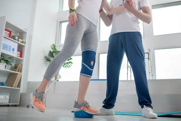 Fotografía del cuerpo inferior de una Mujer en rehabilitación de su rodilla en la clínica de rodillas con ayuda profesional